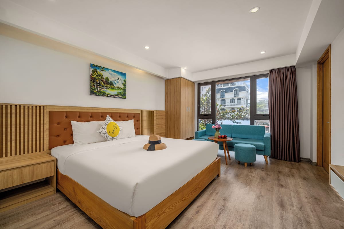 A modern hotel room with a large bed, wooden headboard, and a view of a building through a large window.