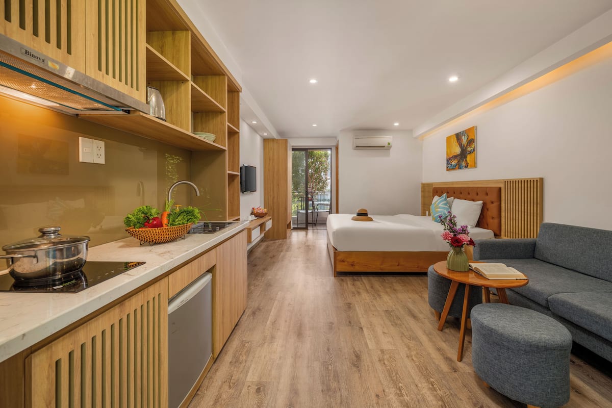 A modern hotel room with a kitchen, a bed, and a seating area.