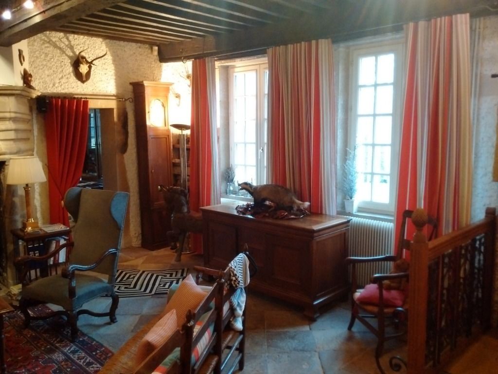 Una habitación tradicional con un escritorio de madera, una silla, un tapete estampado y un gran ventanal con cortinas.