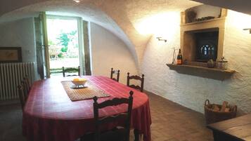 A dining area with a red tablecloth, wooden chairs, a fireplace, and a basket of firewood.