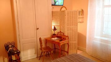 A room with a wooden desk, two chairs, a television on the wall, a wicker screen, and a window with curtains.