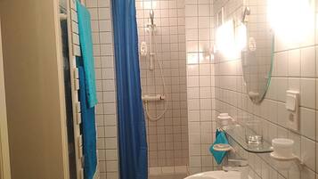 A small bathroom with white tiled walls, a white sink, a blue shower curtain, and a glass shower door.