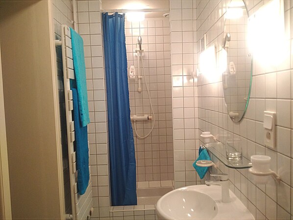 A small bathroom with white tiled walls, a white sink, a blue shower curtain, and a glass shower door. - Chambres d'hôtes Le Prieuré (Aydoilles)