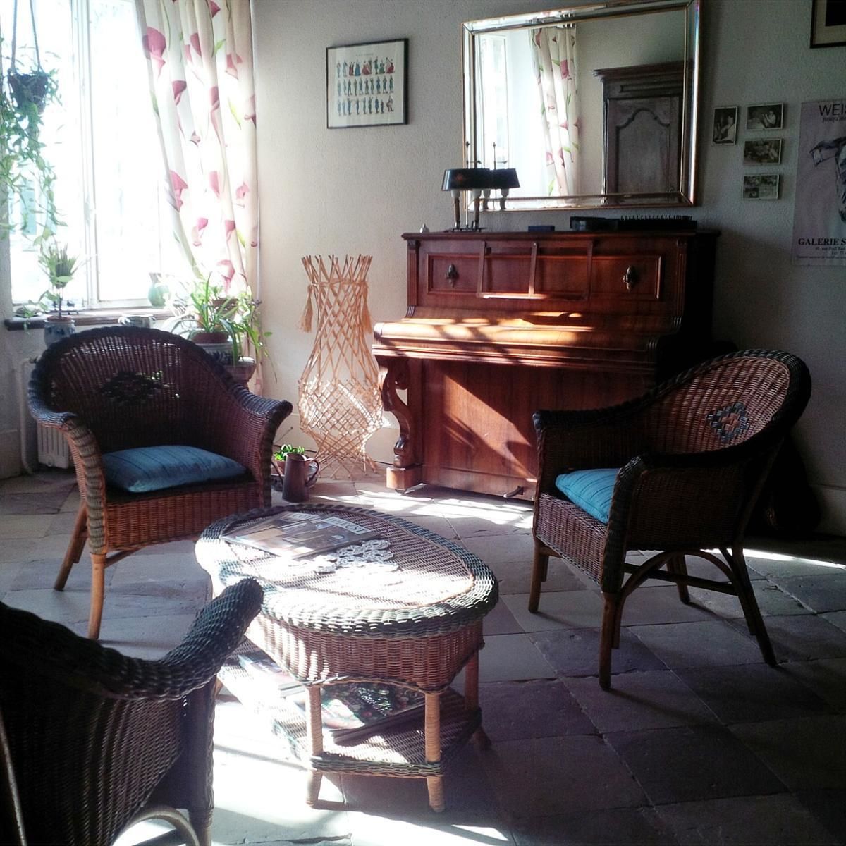 Een zonnige kamer met rieten meubels, een houten kast en een grote spiegel.