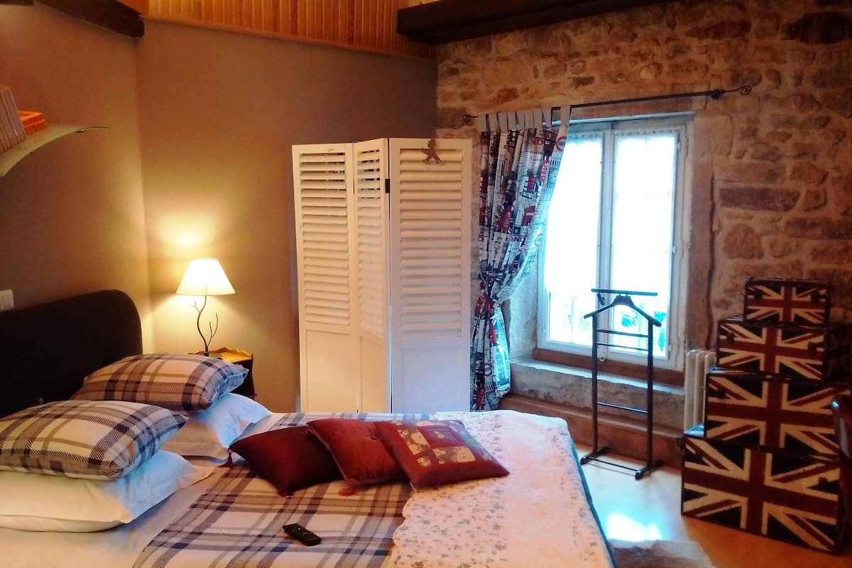 Quarto com cama, almofadas, luminária, guarda-roupa, janela com cortinas e radiador.