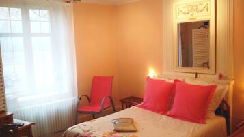Ein Schlafzimmer mit einem Bett, einem Sessel, einem kleinen Tisch und einem Fenster mit Vorhängen.