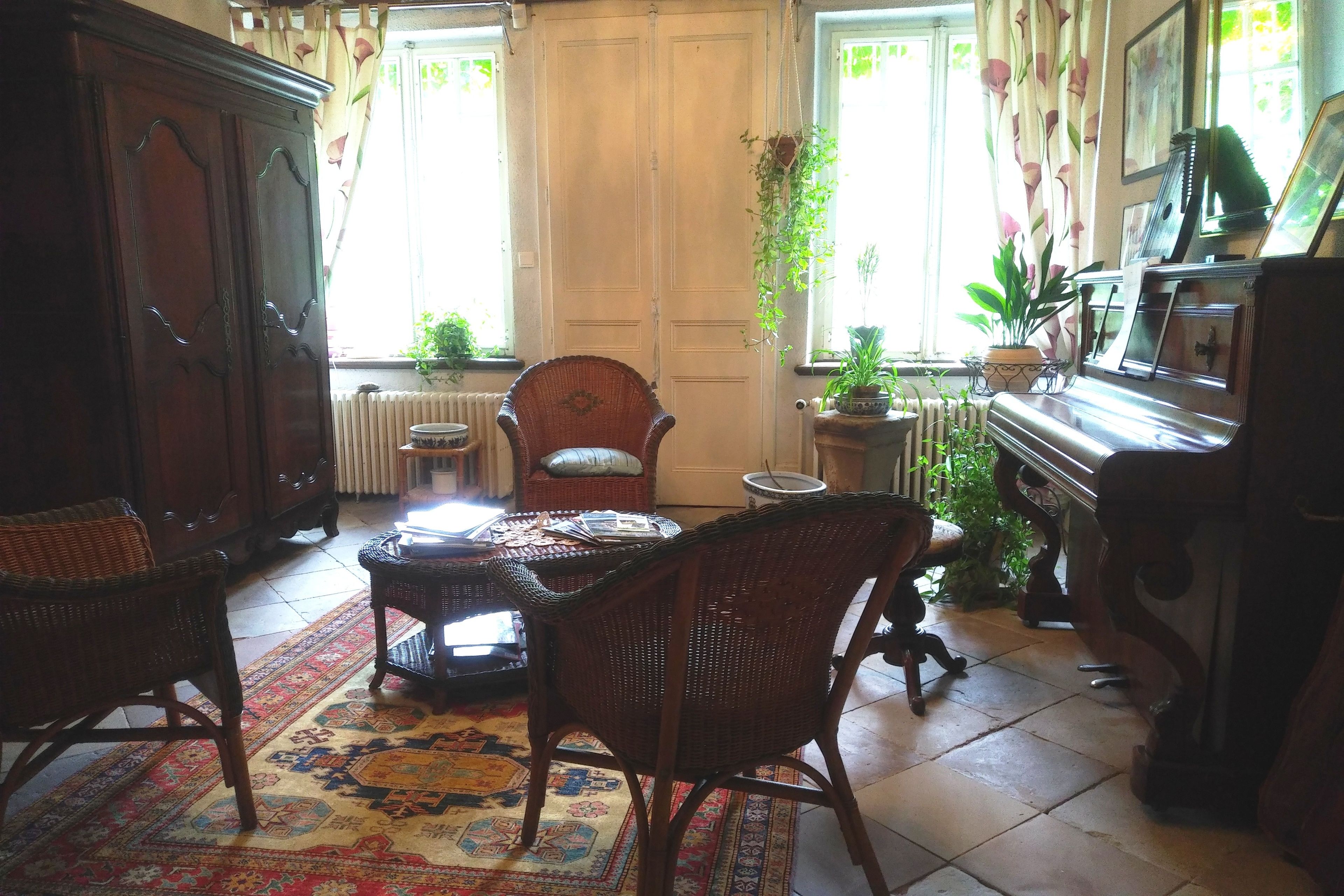 Une pièce au décor traditionnel, avec un meuble en bois, des chaises en osier, un tapis à motifs, un piano et des plantes en pot.