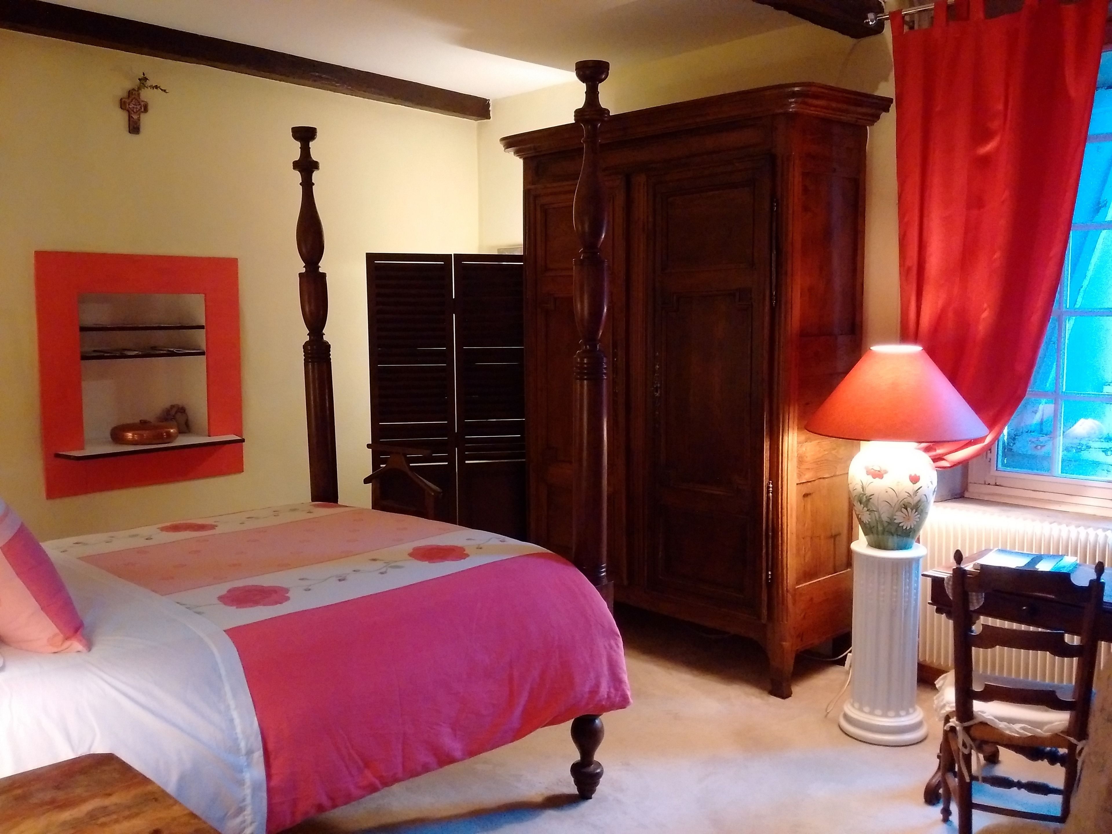 Ein Schlafzimmer mit einem Bett, einem Holzschrank, einem roten Vorhang und einer Tischlampe.