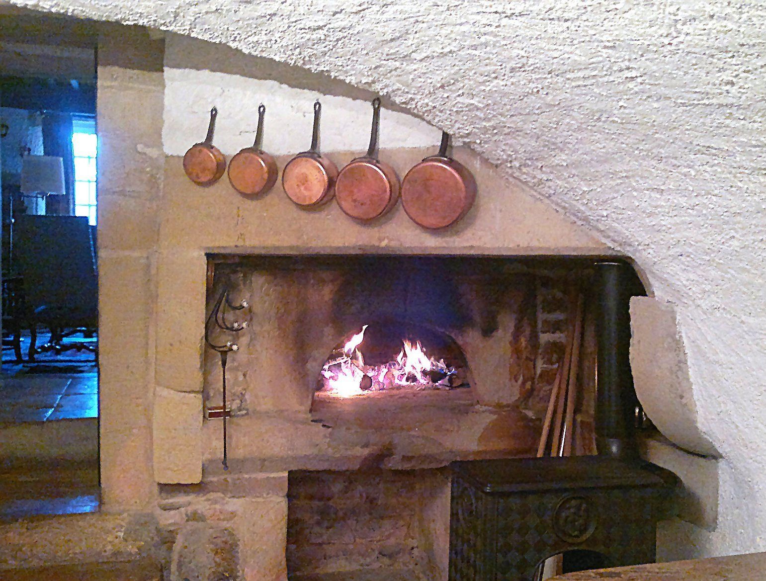 A stone fireplace with a fire, a metal rack with pots above it, and a stone wall.