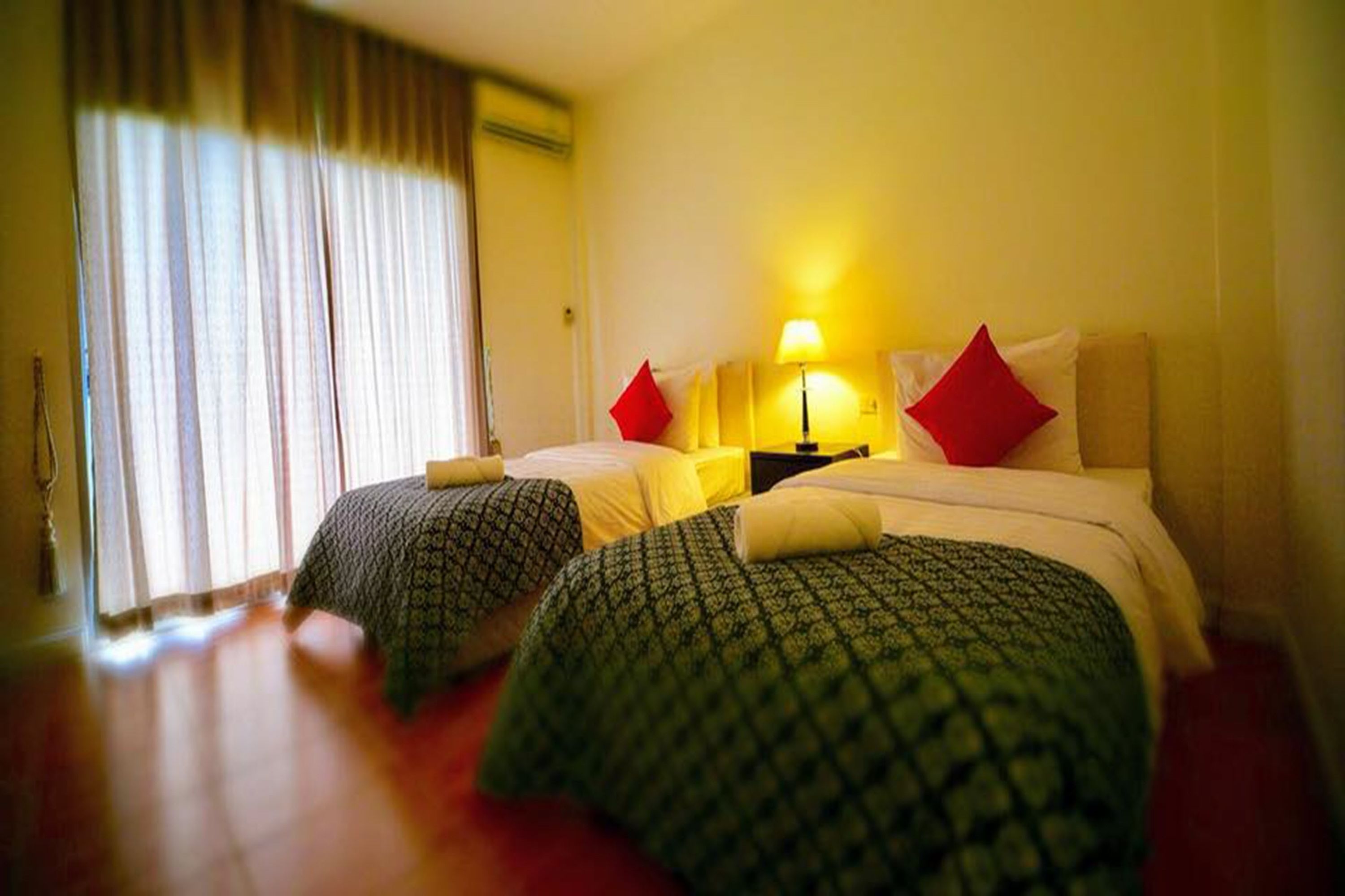 Habitación de hotel con dos camas, una mesita de noche, una lámpara y una ventana con cortinas.