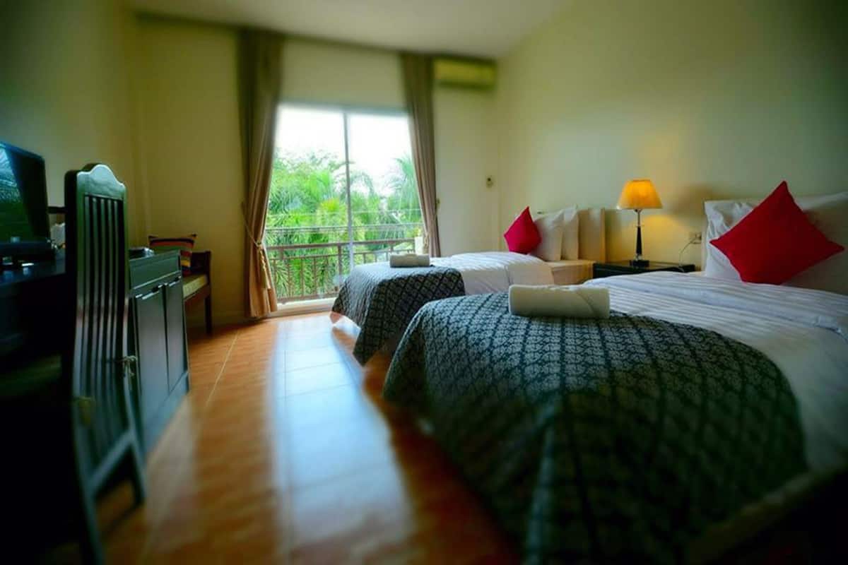 Ein Hotelzimmer mit zwei Betten, einem Fernseher, einem Schreibtisch und einem Balkon mit Blick auf Grünflächen.