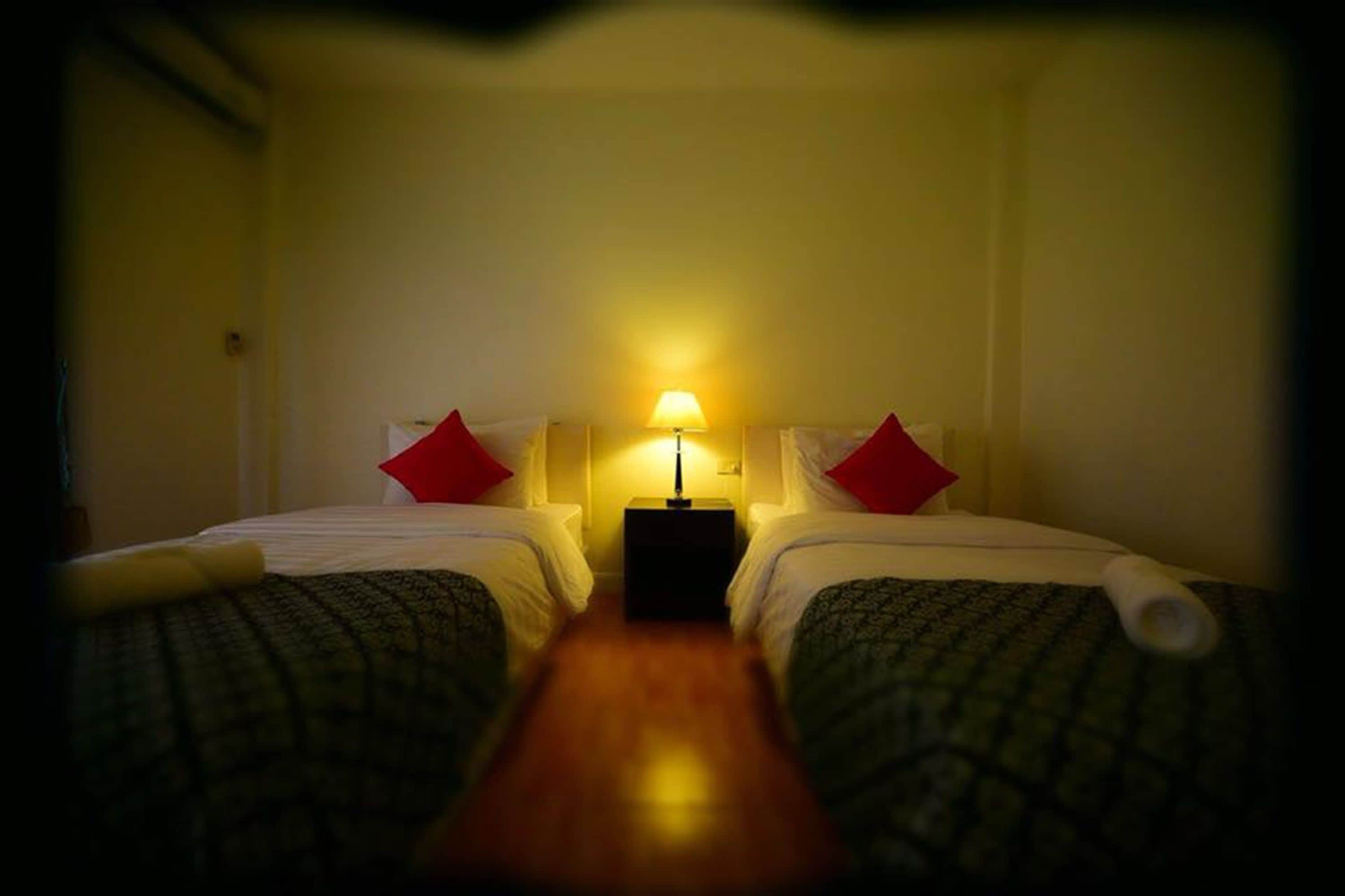 Una habitación de hotel con dos camas, una mesita de noche con lámpara y almohadas rojas.