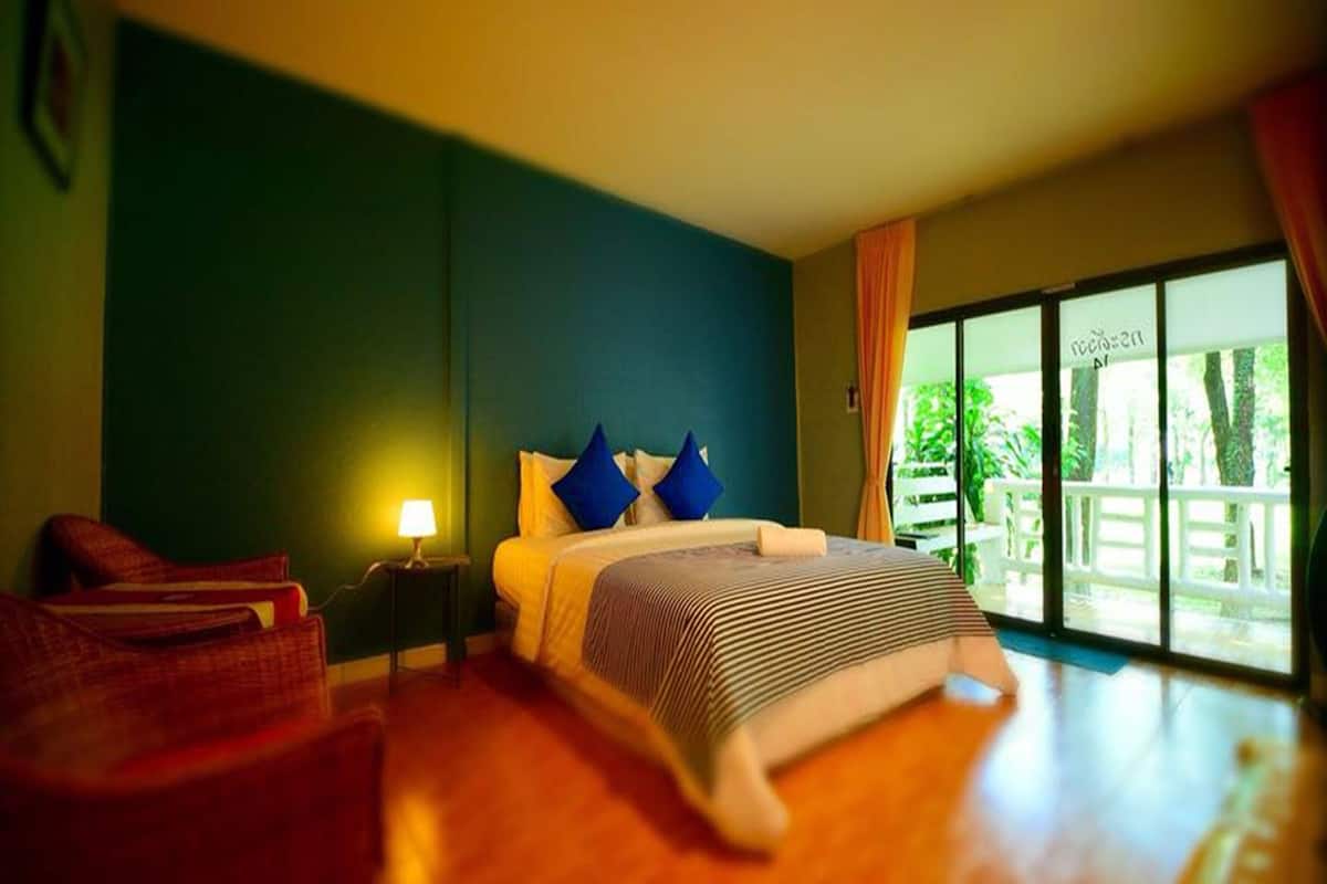 Ein Hotelzimmer mit Bett, Stuhl, Nachttisch und Blick ins Freie.