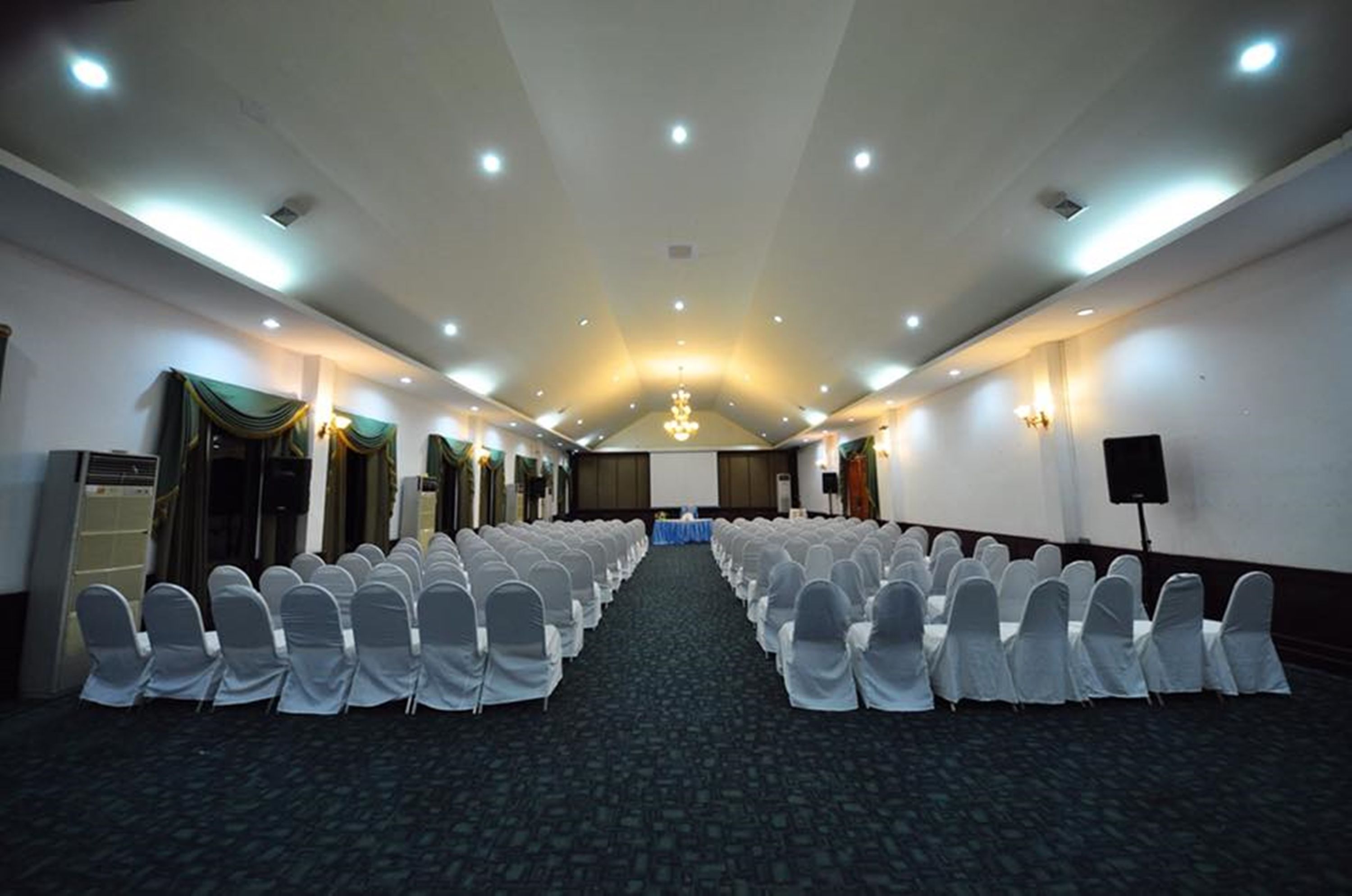 A conference room with rows of chairs, a projector screen, and a stage at the front.