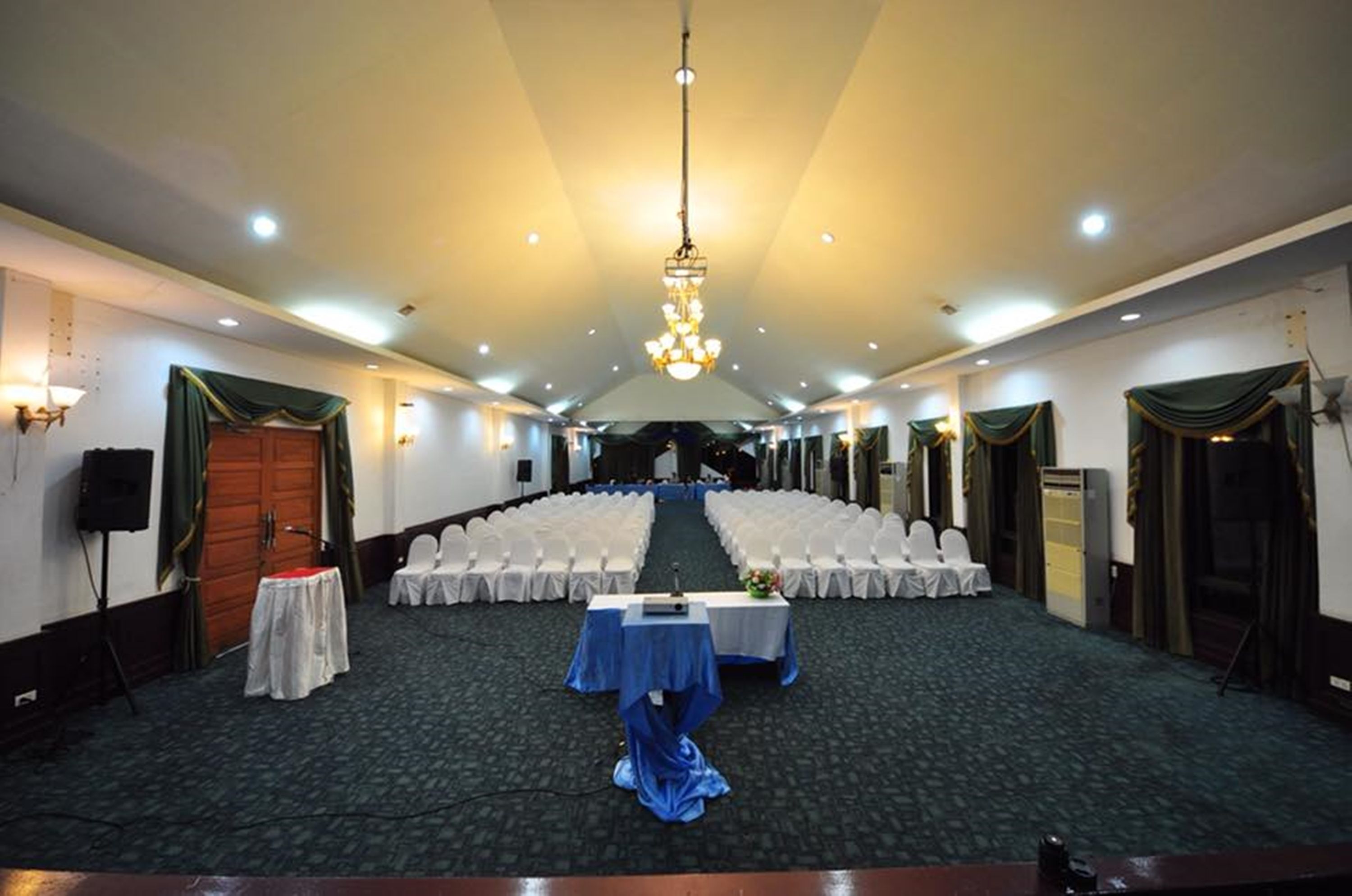 A conference room with rows of white chairs, a stage, and a chandelier.