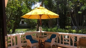 Een terras met twee blauwe loungestoelen, een houten tafel en een gele parasol.
