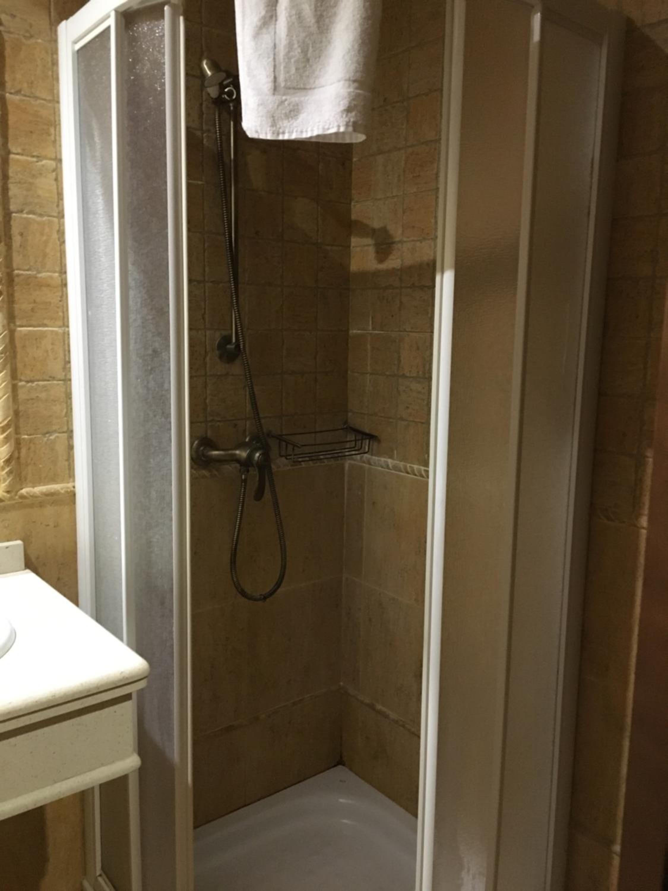 A small, enclosed shower area with a white sink and a towel hanging on the wall.