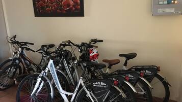 Varias bicicletas aparcadas en un interior, un cuadro eléctrico sujeto a la pared y una obra de arte enmarcada.
