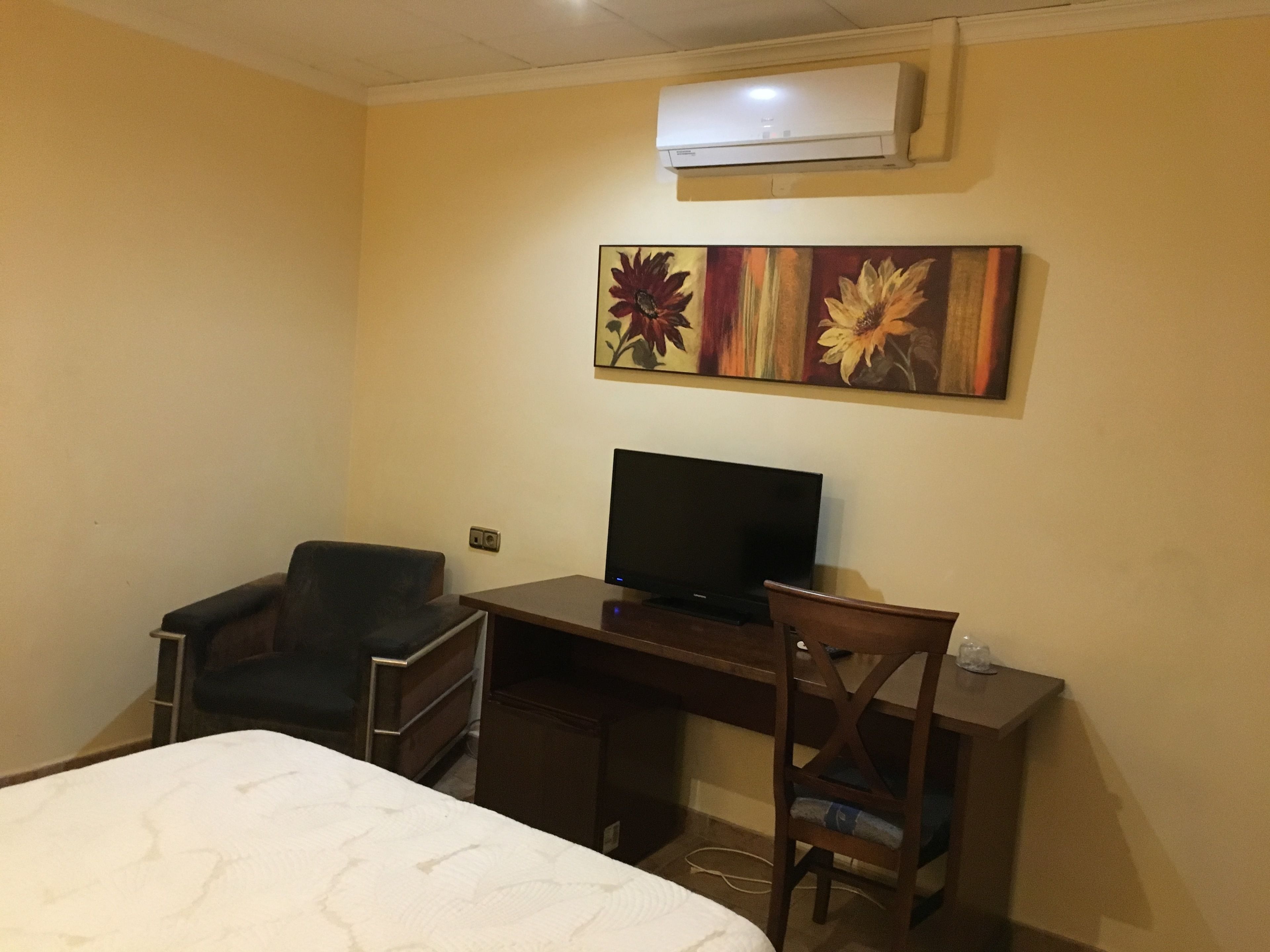 Une chambre d’hôtel avec un lit, un bureau équipé d’un ordinateur, une chaise et un appareil de climatisation fixé au mur.