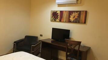 Une chambre d’hôtel avec un lit, un bureau équipé d’un ordinateur, une chaise et un appareil de climatisation fixé au mur.