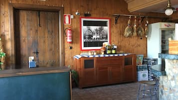 A wooden interior with a reception desk, a fire extinguisher, a framed photograph, and a bar area with stools.
