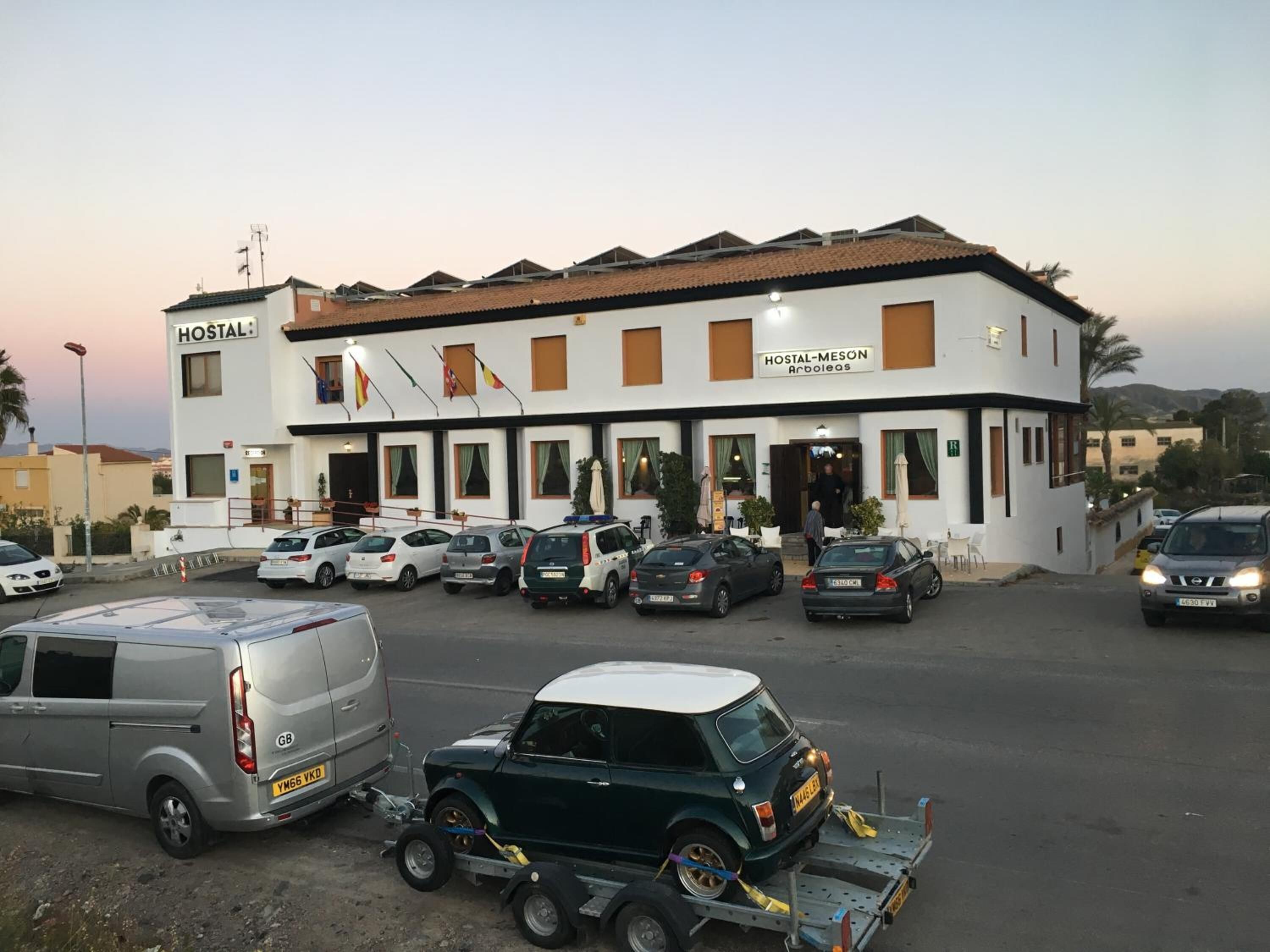 A building labeled "HOSTAL-MESON Arboleda" with multiple cars parked in front.