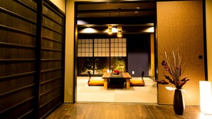 Ein traditioneller japanischer Raum mit Tatami-Boden, einem niedrigen Tisch mit Kissen und einer Vase mit Trockenpflanzen.