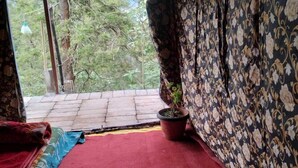 A room with a red carpet, a patterned curtain, and a view of greenery outside. - Janardan Tea Resort - Campsite (Kunda)