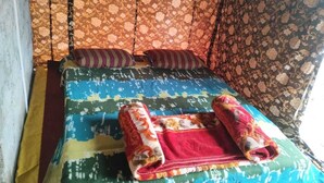 A bed with a colorful bedspread and two rolled-up towels. - Janardan Tea Resort - Campsite (Kunda)