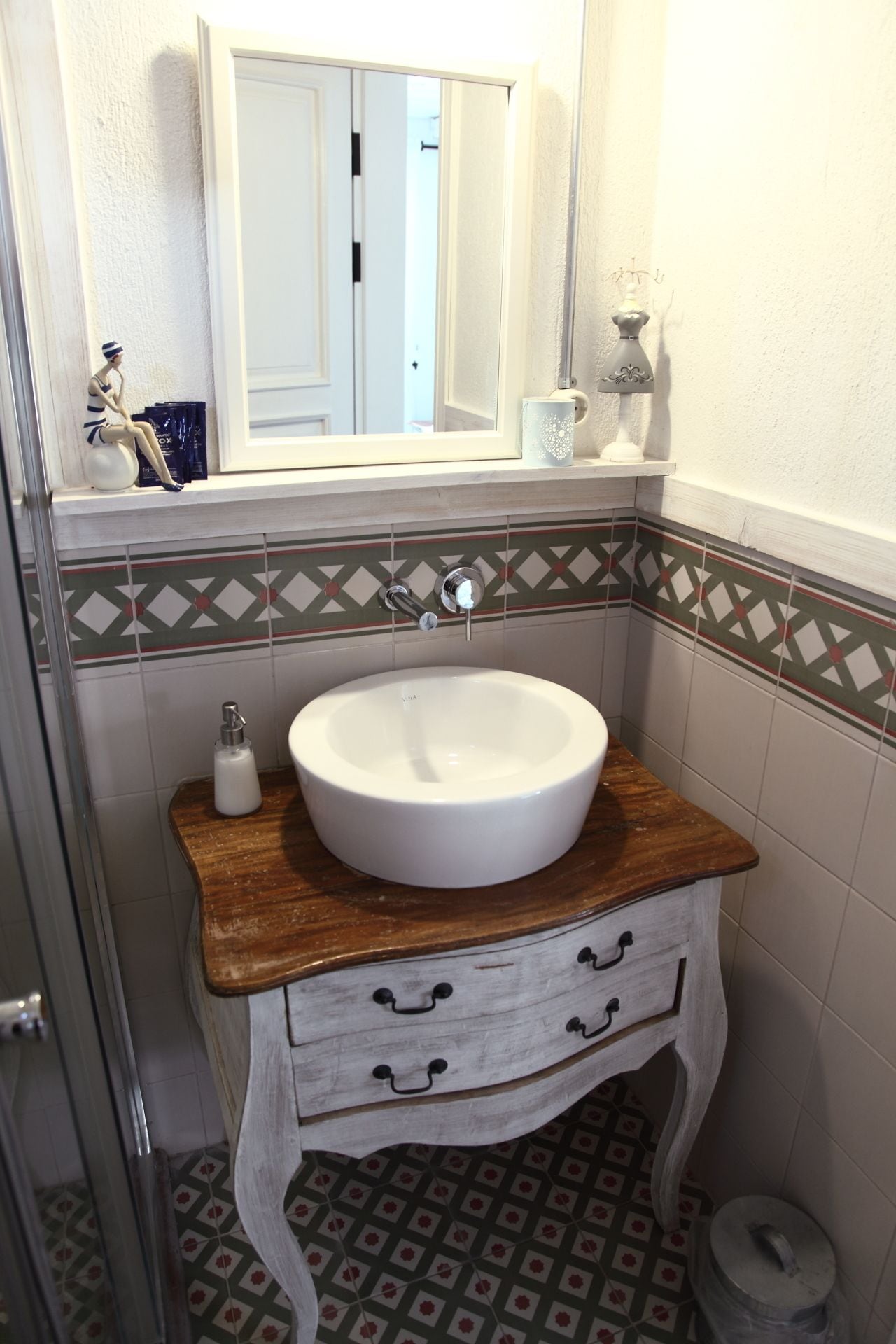 A bathroom with a white sink, wooden vanity, patterned tiles, and a mirror above the sink.