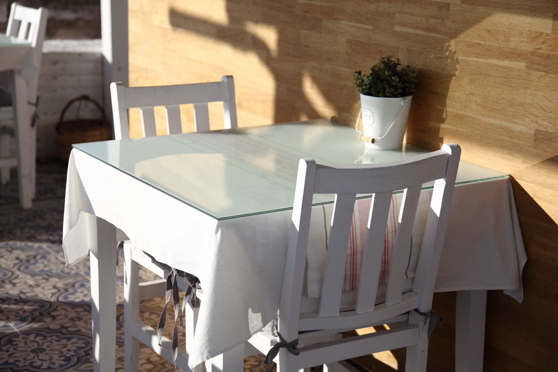 Ein Esstisch mit Glasplatte, umringt von weißen Stühlen. Auf dem Tisch steht ein Blumentopf.