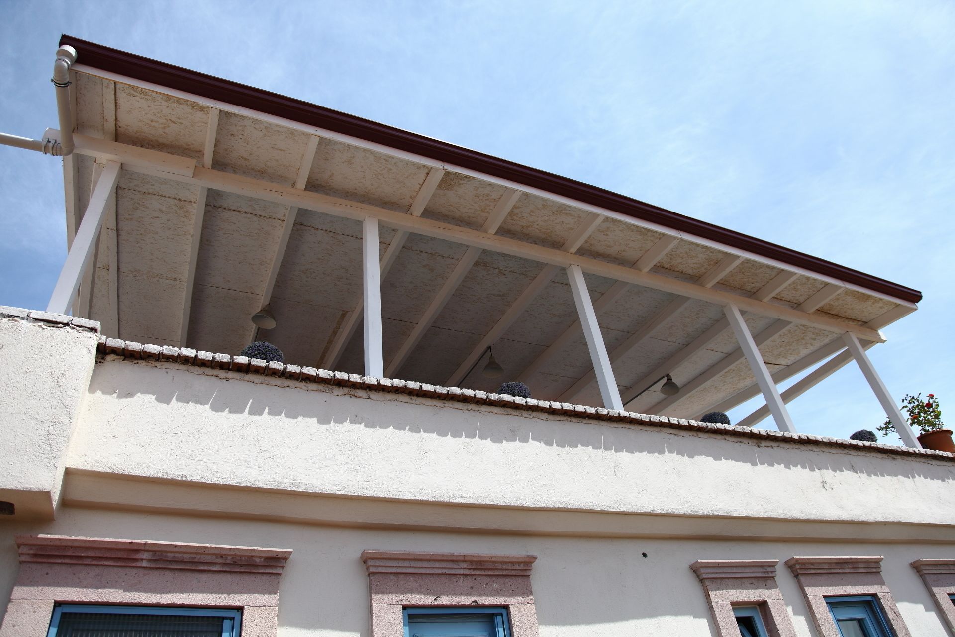 A building with a flat roof, white walls, and a balcony with a wooden railing.