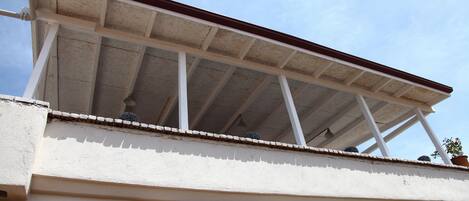 A building with a flat roof, white walls, and a balcony with a wooden railing.