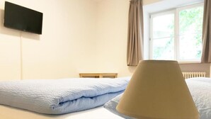 A bed with a blue blanket and a lamp on a bedside table in a room with a window and a radiator. - Manzoni Premium (Merano)