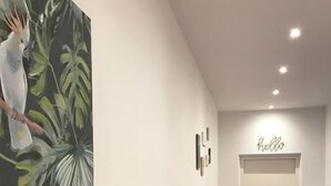 A hallway with a red carpet, a white door with a 'hello' sign, and a wall with a bird painting. - Manzoni Premium (Merano)