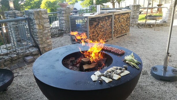 A round outdoor grill with sausages, vegetables, and wood burning. - Landhotel Schloss Sörgenloch (Sörgenloch)