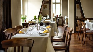 A dining area with wooden chairs and tables set for a meal, featuring a white tablecloth and a vase with flowers. - Landhotel Schloss Sörgenloch (Sörgenloch)