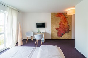 Habitación de hotel con cama, dos sillas, escritorio con televisor y un cuadro grande de un pez en la pared.