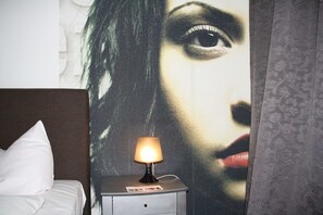 Una habitación de hotel con una cama, una mesita de noche con lámpara y un mural grande en la pared.