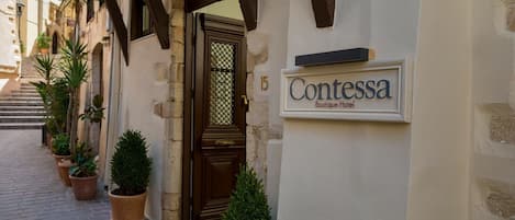 A narrow alley with a boutique hotel entrance, potted plants, and a sign for 'Contessa Boutique Hotel'.