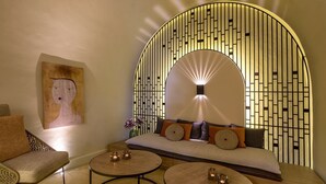 A modern lounge with a sofa, two round tables, and a decorative wall with a light fixture. - Contessa Boutique Hotel (Chania)