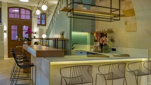 A modern kitchen with a central island, bar stools, and a staircase leading to an upper level. - Contessa Boutique Hotel (Chania)