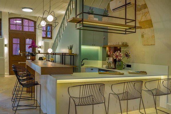 A modern kitchen with a central island, bar stools, and a staircase leading to an upper level. - Contessa Boutique Hotel (Chania)