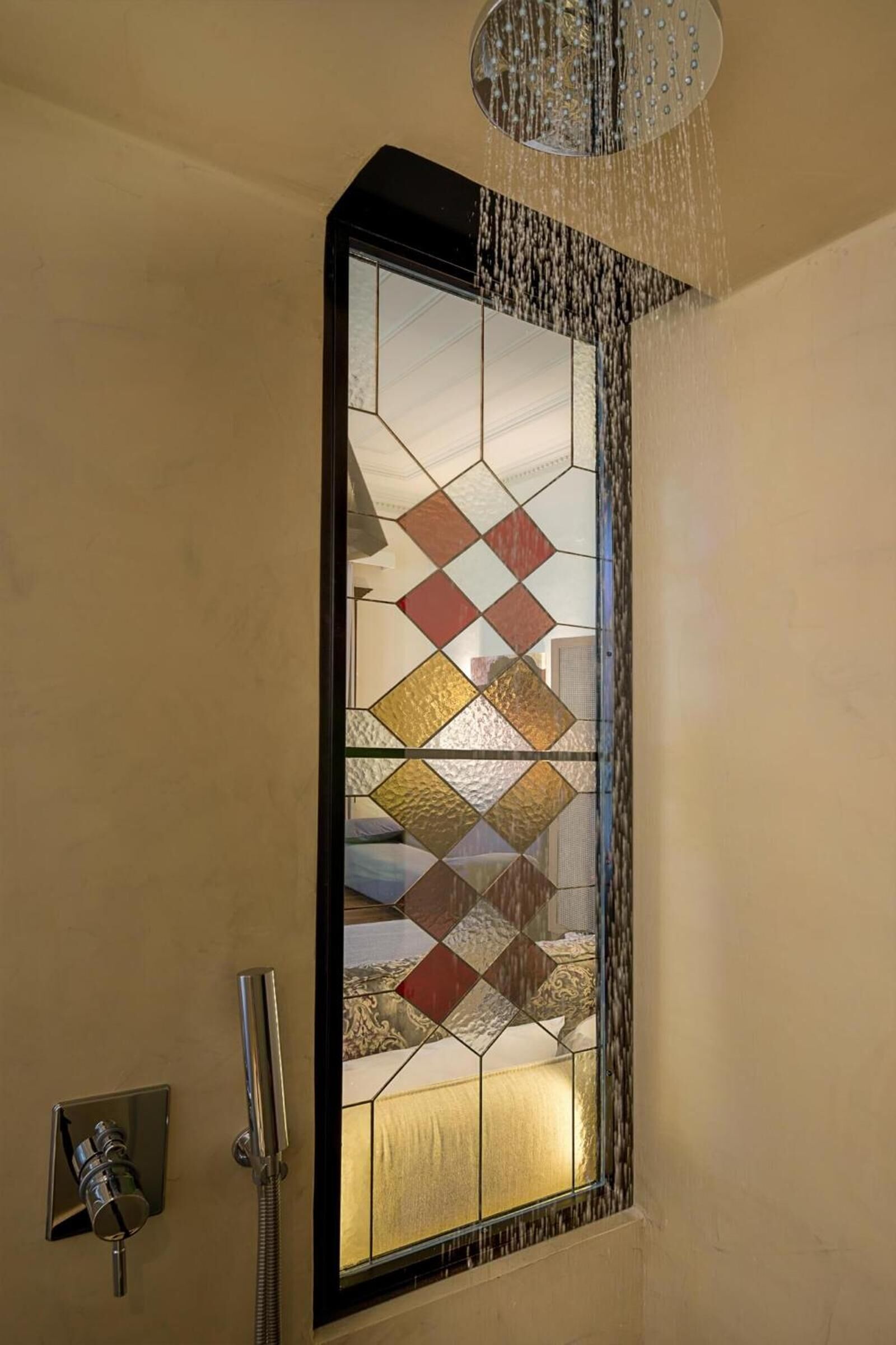 A shower with a stained glass window, a showerhead, and a control panel.