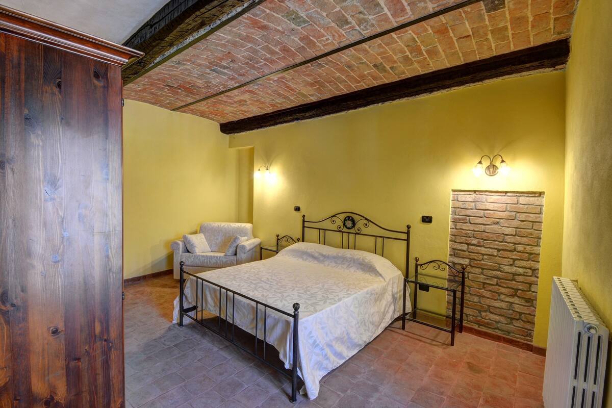 A bedroom with a bed, a chair, a stone wall, and a radiator.