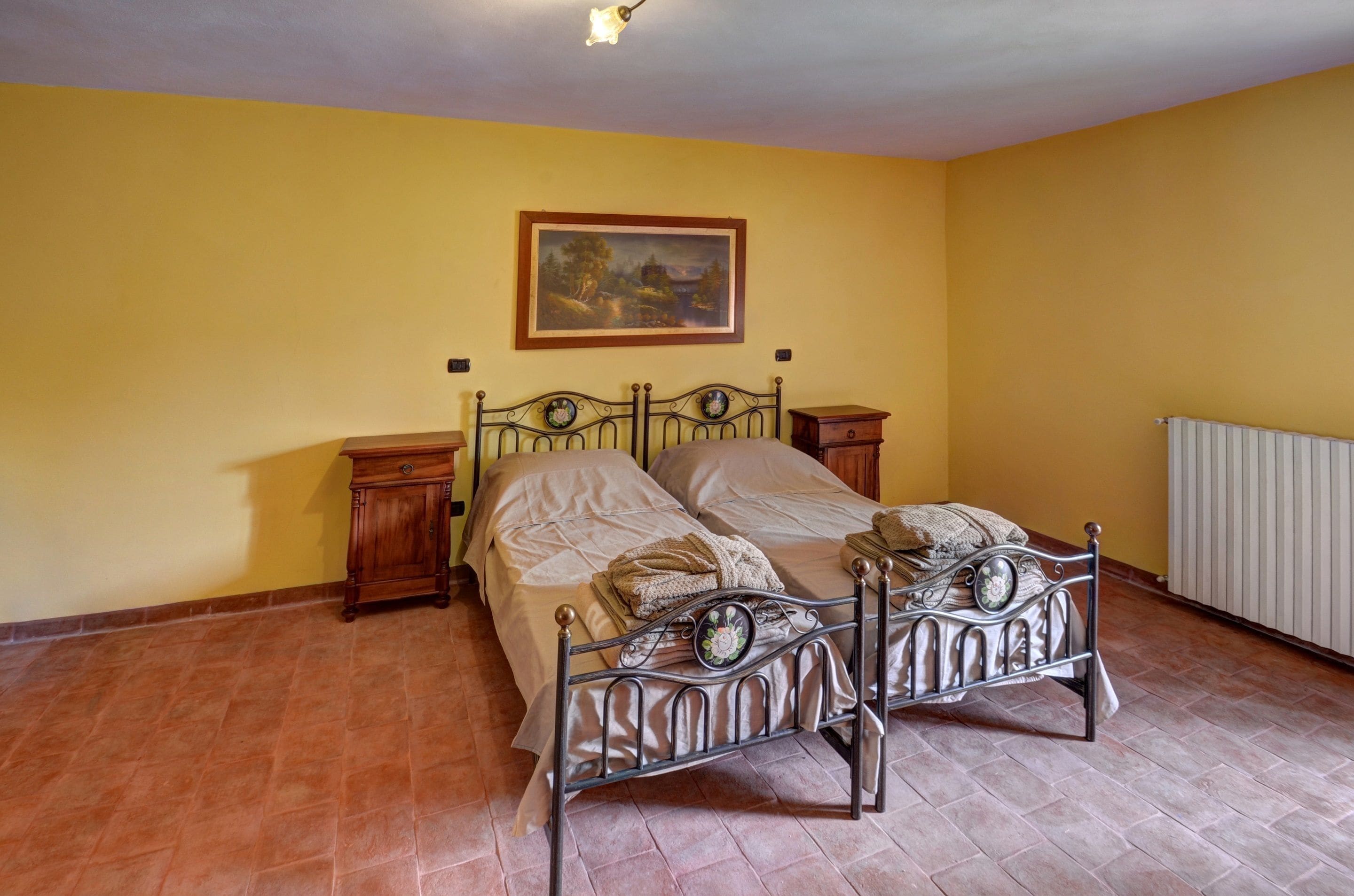 A bedroom with a metal bed frame, two bedside tables, a wooden cabinet, and a radiator.