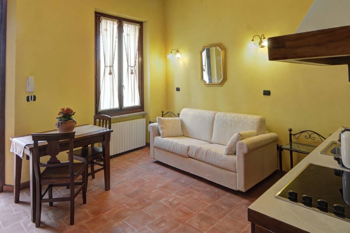 A yellow-walled room with a dining table, a white sofa, a radiator, and a ceiling fan.