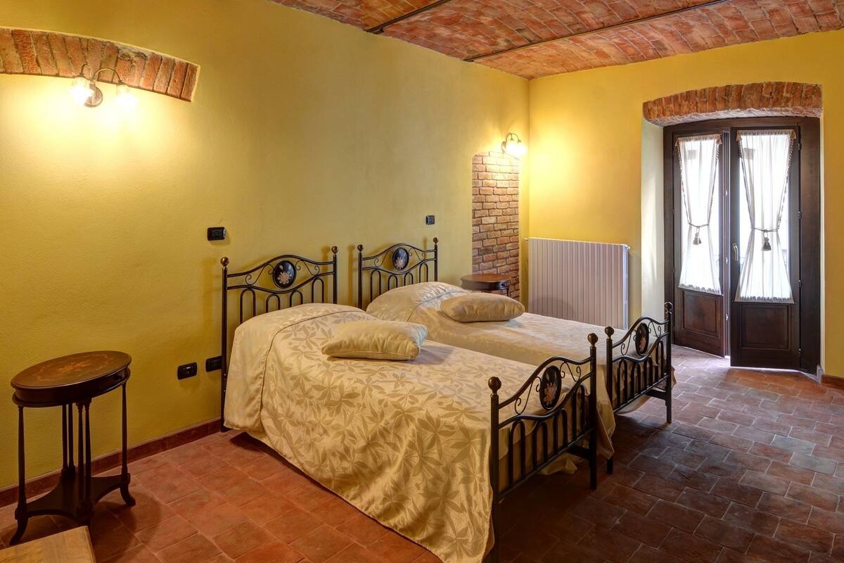 A bedroom with a brick ceiling, two beds, a small table, and a door with curtains.