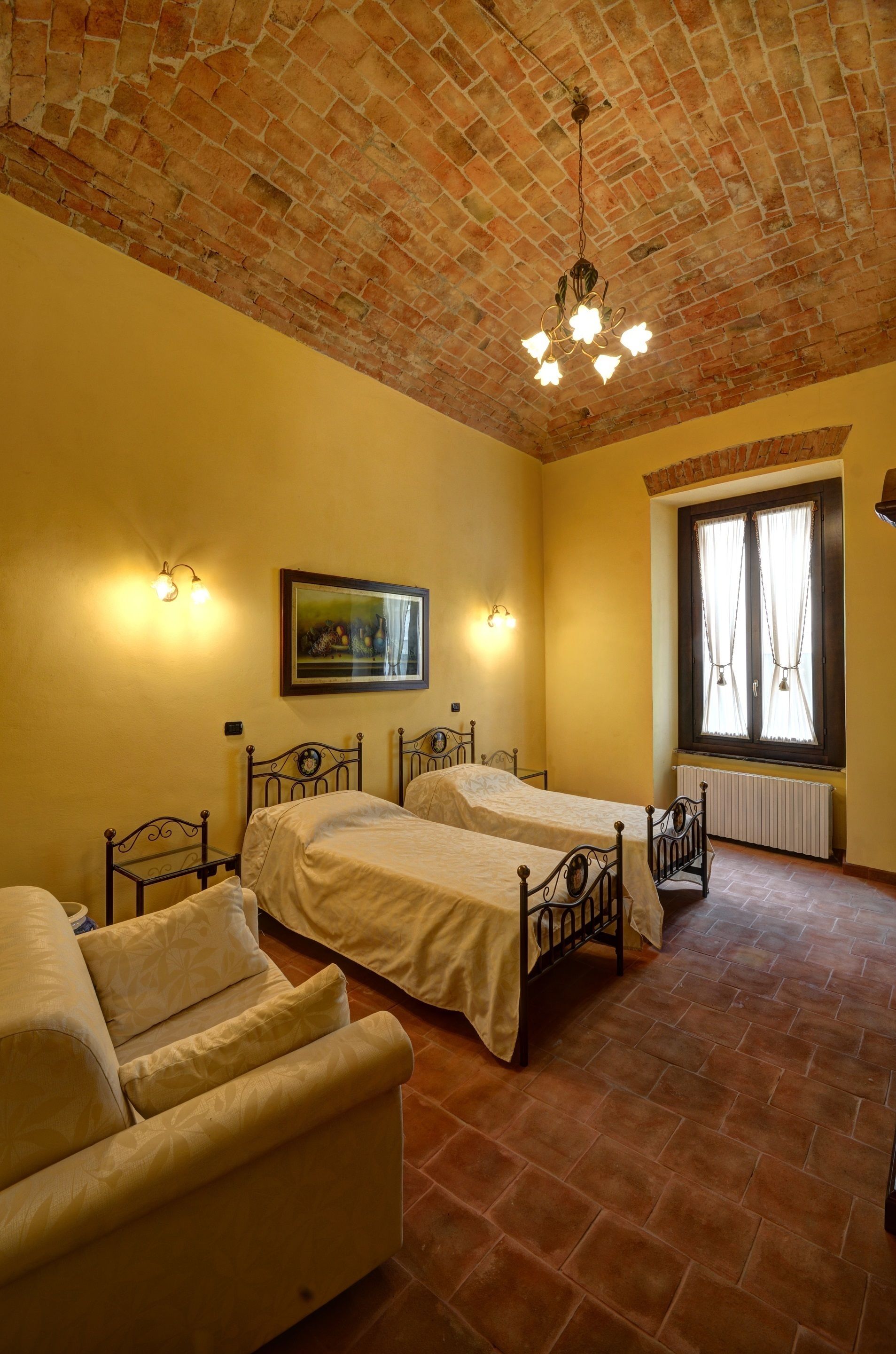 A room with two beds, a sofa, a brick ceiling, and a window with curtains.