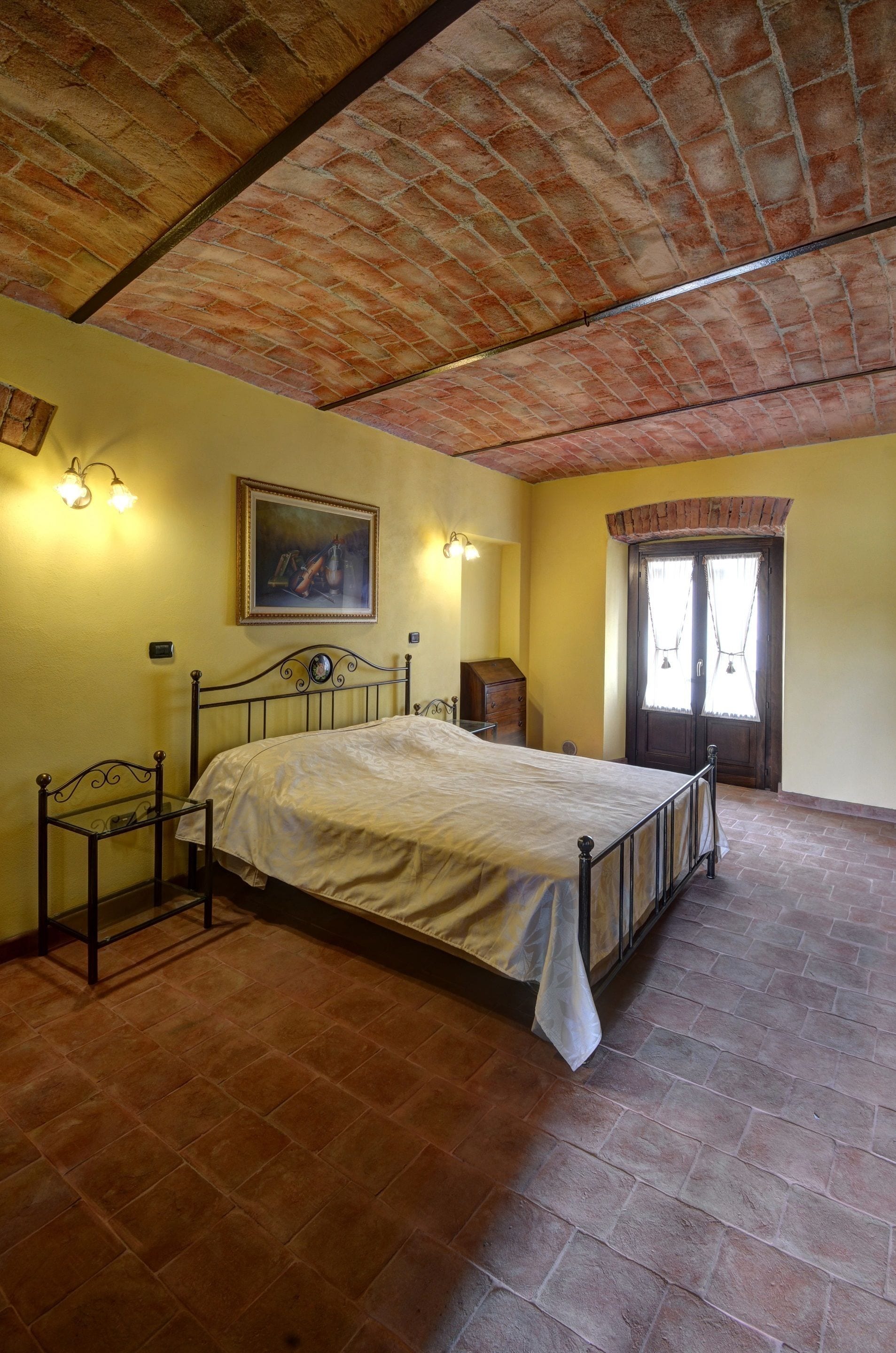 A bedroom with a brick ceiling, a bed, a nightstand, a dresser, and a door with curtains.